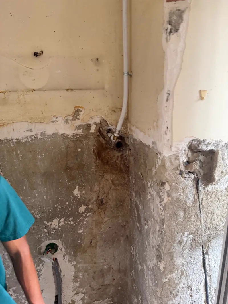 Dépose d'un ancien raccord d'évacuation sur un mur dégradé par l'humidité